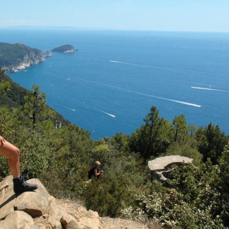 Woman gazes at the blue Mediterranean from a rocky summit.