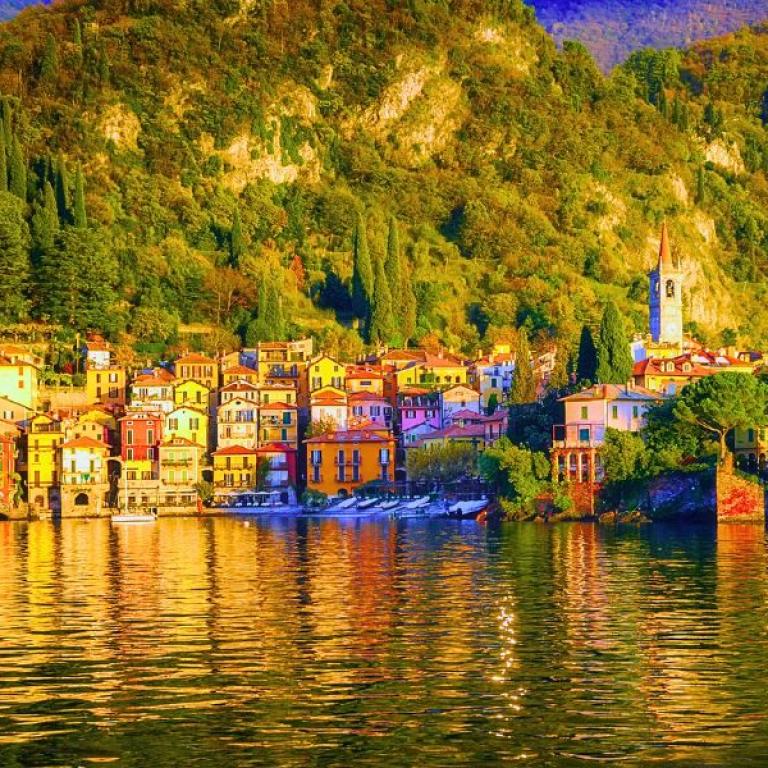 Borgo colorato sul Lago di Como con campanile e colline verdi riflesse nell’acqua