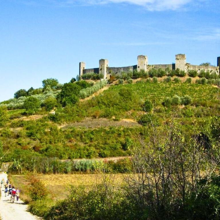 People walking on an unpaved walking path toward Monteriggioni