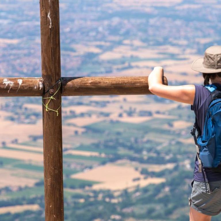 Hiker beside a wooden cross overlooking the valley along the St Francis Way