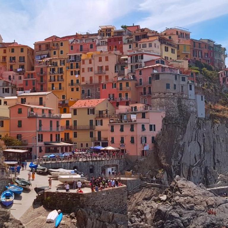 Manarola’s pastel houses clinging to the rocky coastline on a sunny day in the Cinque Terre