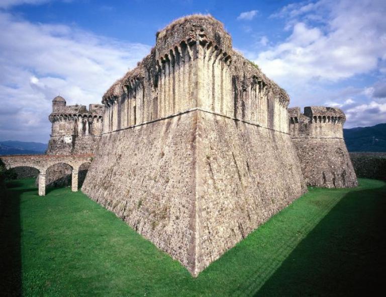 Impressive stone fortress of Sarzanello surrounded by green lawns on a bright day in Liguria