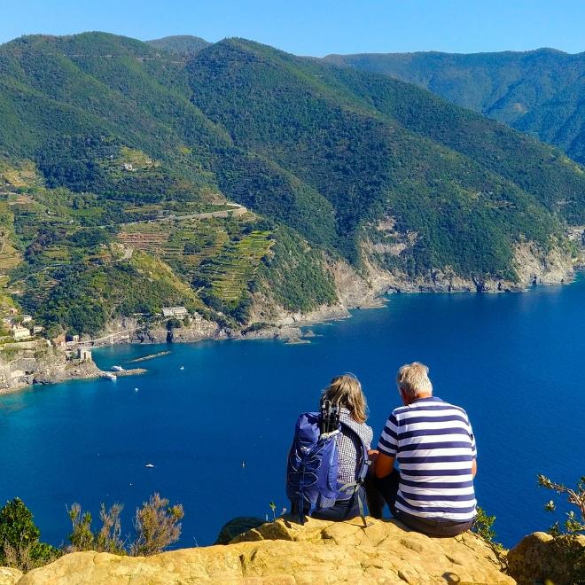 Couple resting on a cliffside viewpoint above the Ligurian Sea along a peaceful hiking path in Cinque Terre