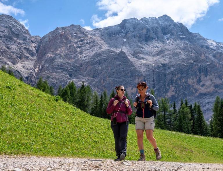 Dos mujeres caminando entre prados y bosques en las Dolomitas, disfrutando de un tranquilo senderismo en Italia