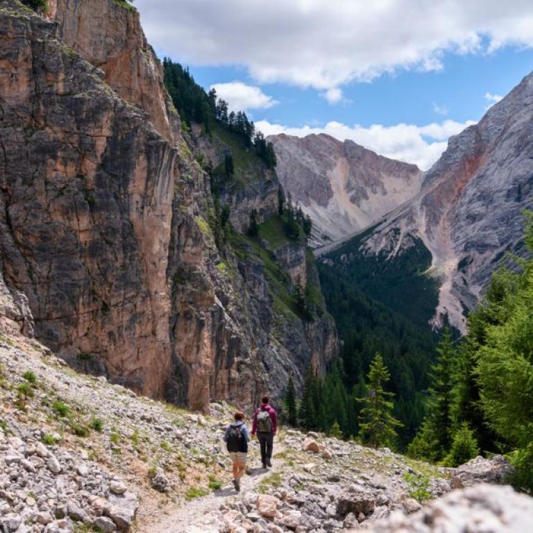 Excursionistas caminando por un sendero rocoso entre los valles de las Dolomitas, disfrutando del senderismo en Italia