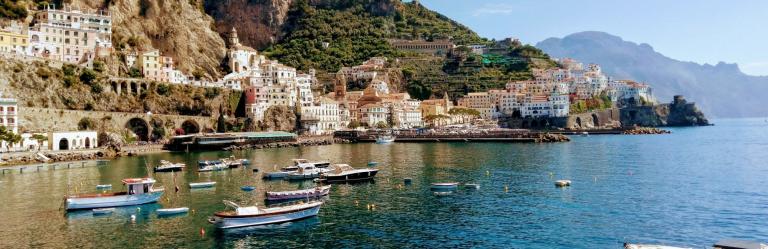 Colorful Amalfi houses rising over the bay with boats floating on calm waters during Amalfi Coast hiking tours.