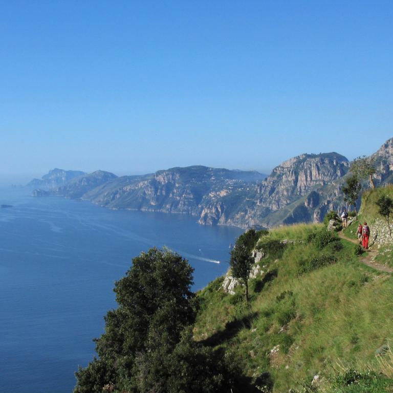 Hikers walking a green cliffside trail overlooking the coastline on Amalfi Coast hiking tours.