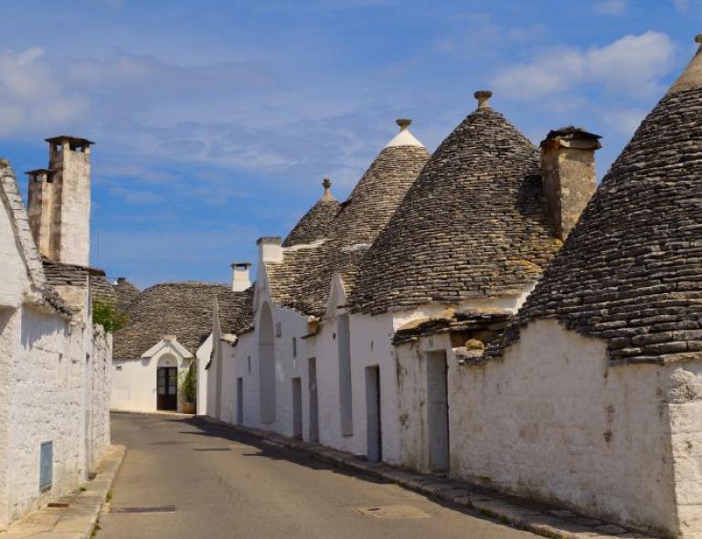 Calle con los tradicionales trulli de Alberobello, símbolo de Puglia – viajes a pie por Puglia y Matera