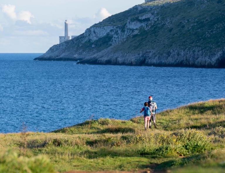 Two hikers walking along the cliffs near Punta Palascia, Southern Italy