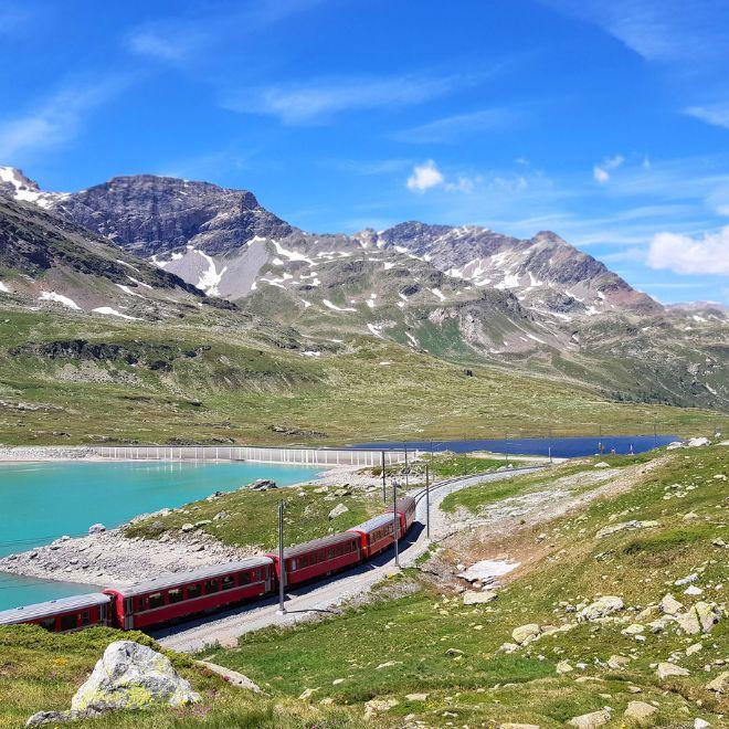 Red Bernina express rolling by lake mountains