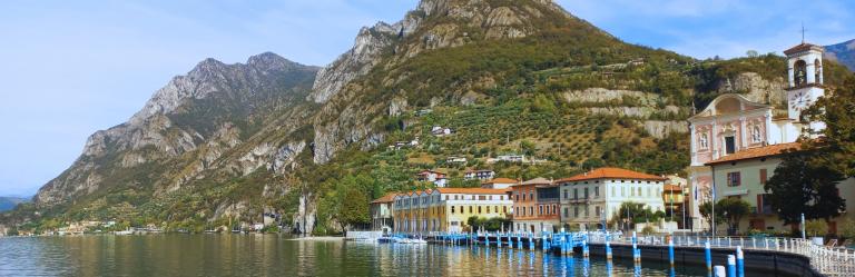 vista panoramica del Lago d’Iseo con il borgo di Iseo affacciato sull’acqua, campanile e case color pastello ai piedi delle montagne.