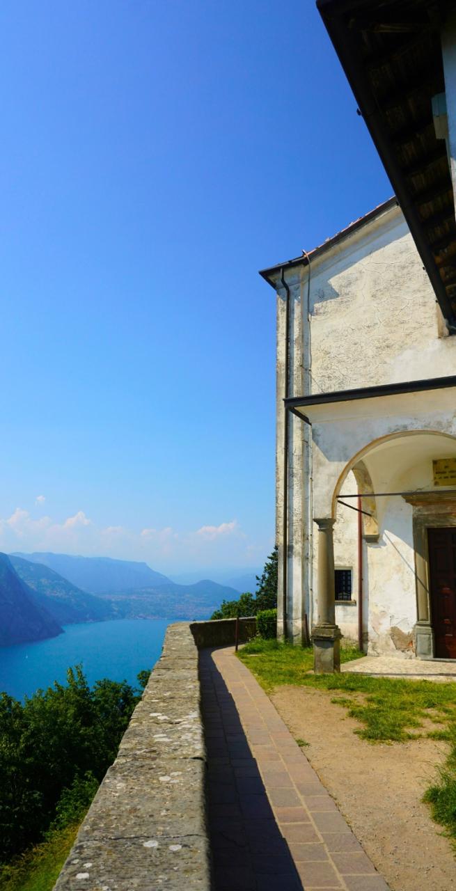 vista panoramica del Lago d’Iseo con il borgo di Iseo affacciato sull’acqua, campanile e case color pastello ai piedi delle montagne.