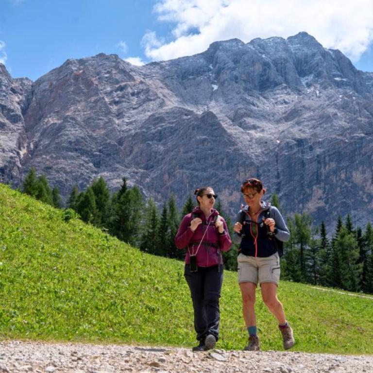 Two women hiking on the Sentiero del Castagno with the Dolomites in the background, enjoying an easy walking holiday in South Tyrol.