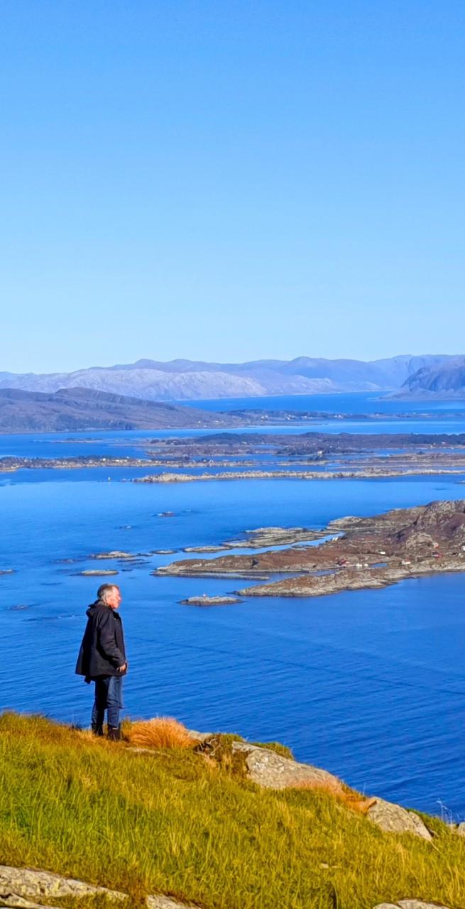 Viandante che ammira il panorama di isole e fiordi dalla costa lungo il Cammino Costiero di Sant’Olav