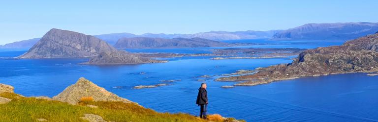 Viandante che ammira il panorama di isole e fiordi dalla costa lungo il Cammino Costiero di Sant’Olav