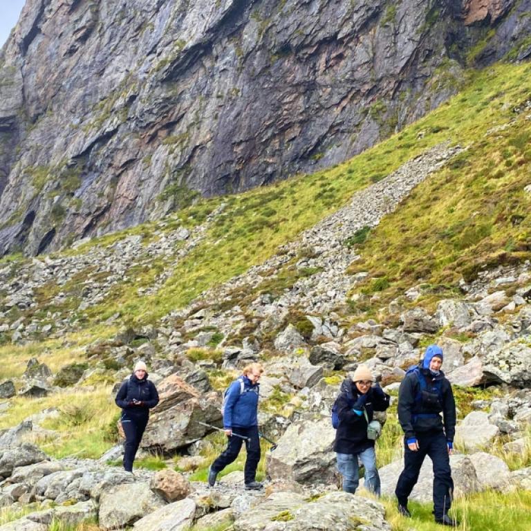 Gruppo di escursionisti su un sentiero roccioso ai piedi delle scogliere lungo il Cammino Costiero di Sant’Olav