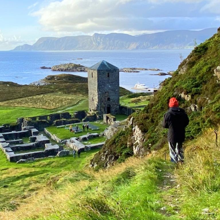 Escursionista in discesa verso le rovine del monastero medievale di Selja lungo il Cammino Costiero di Sant’Olav