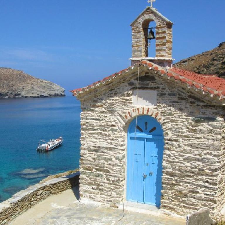 Small white chapel in Andros with a blue door overlooking the Aegean Sea
