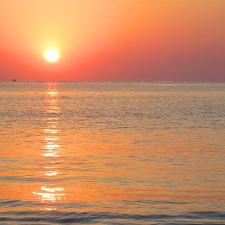 Sunset over the sea with a small lighthouse in the distance in the Cyclades