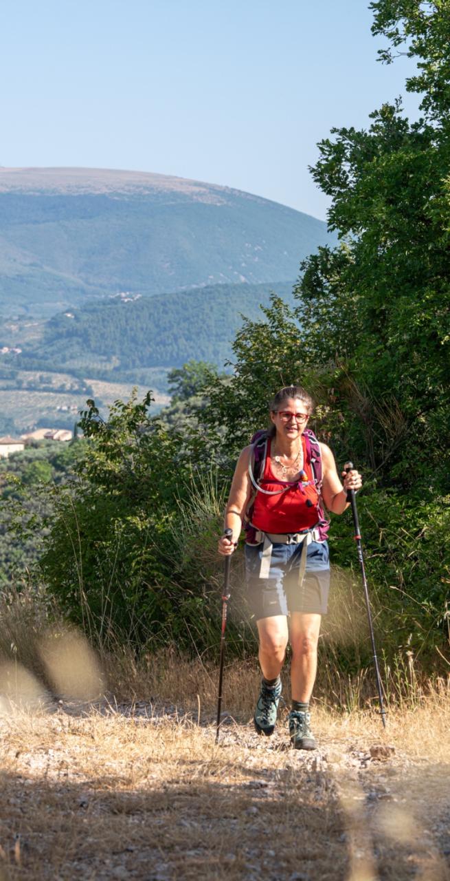 Escursionista lungo un sentiero immerso nella natura sulla Via di Francesco da Firenze a Roma, tra colline e vegetazione mediterranea