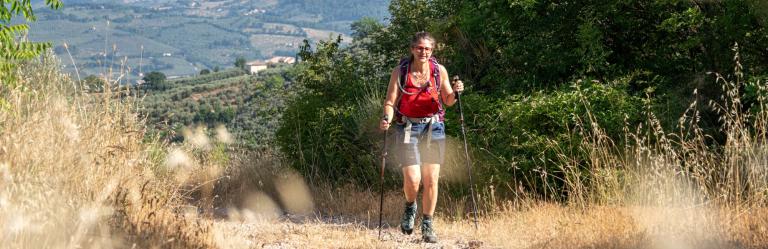 Escursionista lungo un sentiero immerso nella natura sulla Via di Francesco da Firenze a Roma, tra colline e vegetazione mediterranea