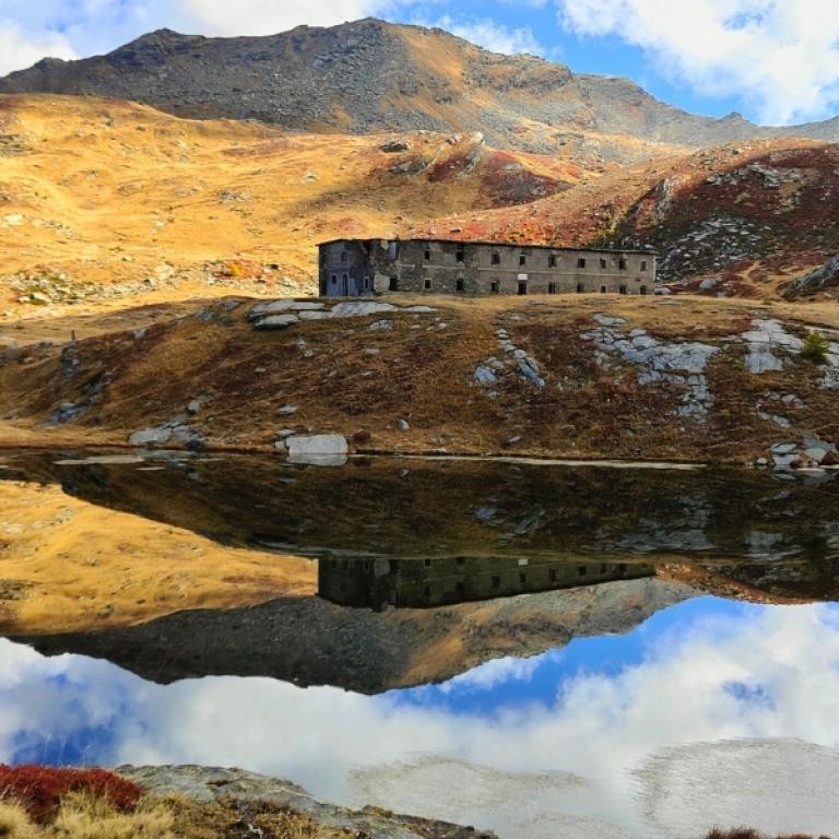 Stone mountain building reflected in a clear alpine lake on the Piedmont alpine walking tour